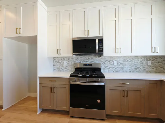 Modern kitchen featuring white shaker-style cabinetry with brushed metal hardware, stainless steel gas range with black front, quartz countertops, and mosaic tile backsplash