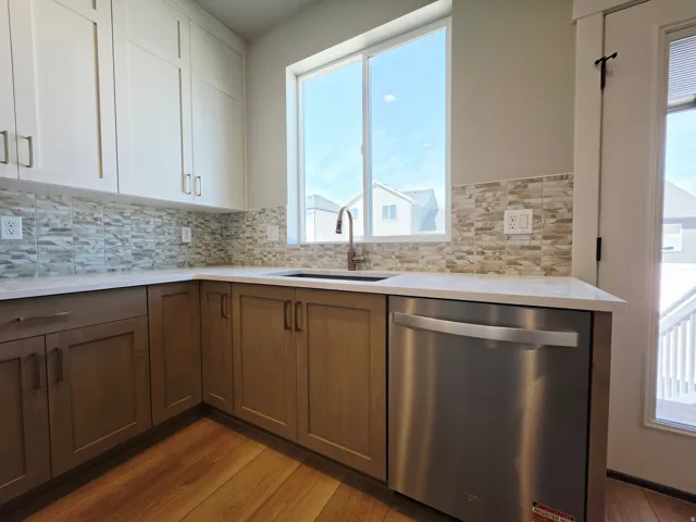 Kitchen featuring two-tone cabinetry, stone tile backsplash, stainless steel dishwasher, and wood-finish flooring