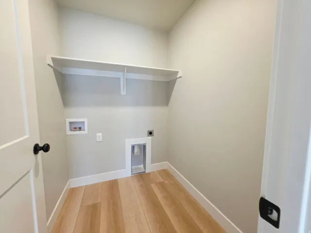 Dedicated laundry area featuring a built-in shelf, wood-finish flooring, and white trim