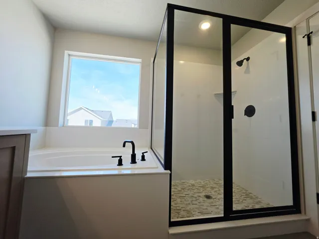 Soaking tub with matte black fixtures, walk-in shower with black-framed glass enclosure, mosaic tile shower floor, built-in shower shelving, and recessed lighting