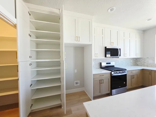 Open pantry shelving, stainless steel appliances, upper cabinetry with gold-finish hardware, lower cabinetry with gold-finish hardware, and a tile backsplash