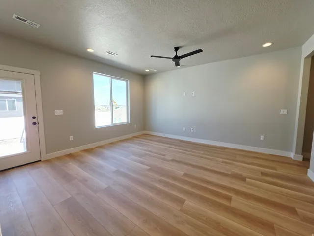 Spacious room featuring wood-finish flooring, recessed lighting, a modern black ceiling fan, and a large window