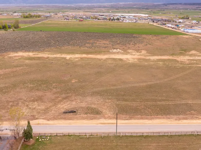 Expansive land parcel featuring a paved road frontage, natural vegetation, and distant community elements