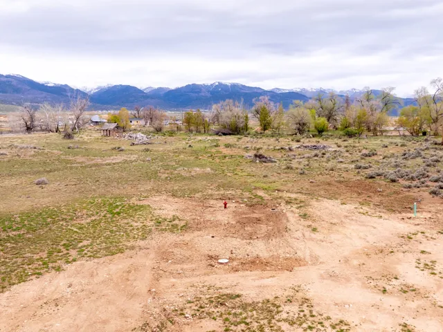 Expansive undeveloped land featuring a cleared building site, mountain backdrop, mature trees, and visible utility connections