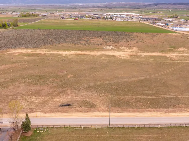 Expansive land parcel featuring a paved road frontage, natural vegetation, and distant community elements