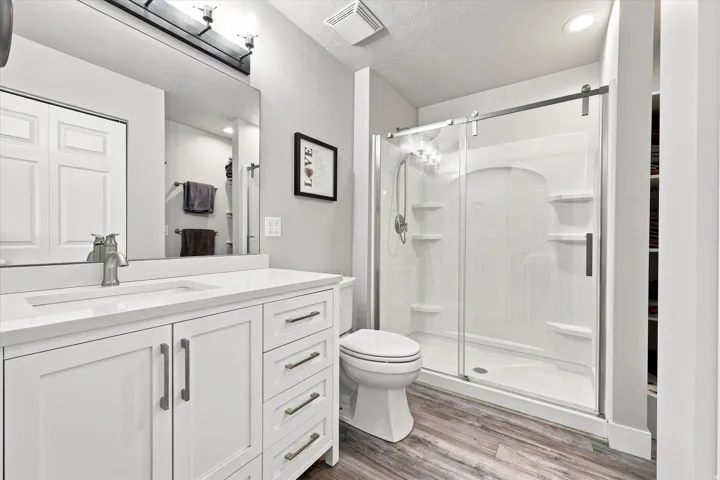 White vanity with integrated sink, wood-finish flooring, glass-enclosed shower with sliding door, and recessed lighting