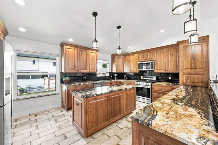 Kitchen featuring extensive wood cabinetry, stone countertops, a central island, stainless steel appliances, and a subway tile backsplash