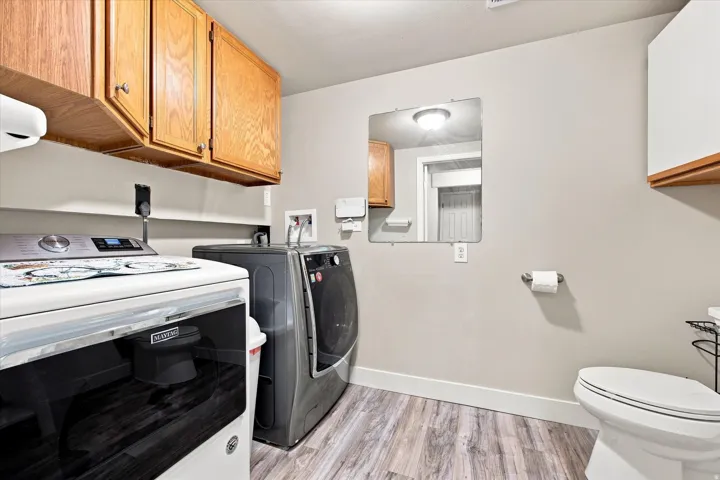 Wood-finish flooring with white trim, wall-mounted cabinetry, and a built-in toilet