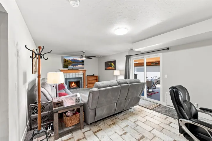 Tile flooring, fireplace with a wood mantel, ceiling fan, and sliding glass door leading to an outdoor space