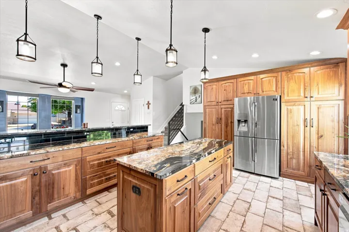 Spacious kitchen featuring two large islands with stone countertops, abundant wood cabinetry, stainless steel refrigerator, and recessed lighting