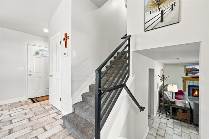 White brick-patterned flooring, contemporary metal stair railing, carpeted staircase, recessed lighting, and a white paneled entry door with frosted glass