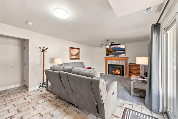 Spacious living area featuring a gas fireplace with tile surround, ceiling fan, wood-finish flooring, and sliding glass doors