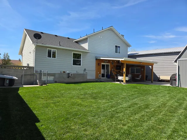 Expansive green lawn, covered patio with wood framing, sliding glass door, and a detached shed