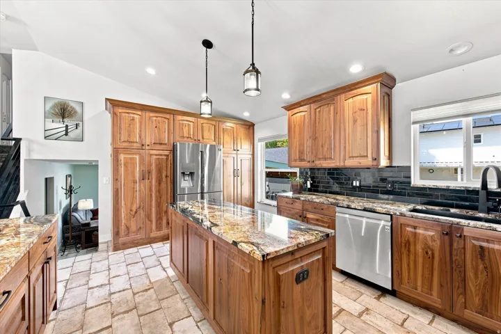 Kitchen featuring wood cabinetry, a center island with a stone countertop, a tile floor, stainless steel appliances, and a black tile backsplash