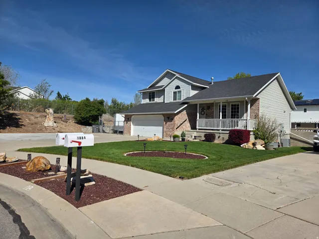 Two-story residence featuring a covered front porch, brick and siding exterior, attached garage, and a landscaped front yard with a manicured lawn