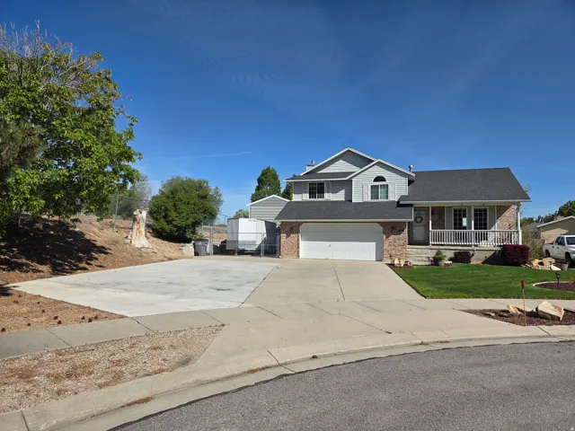 Two-story residence featuring a gray exterior, brick facade, covered front porch, attached two-car garage, and a concrete driveway with additional concrete parking area