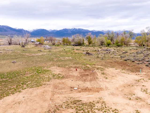 Expansive undeveloped land featuring a cleared building site, mountain backdrop, mature trees, and visible utility connections