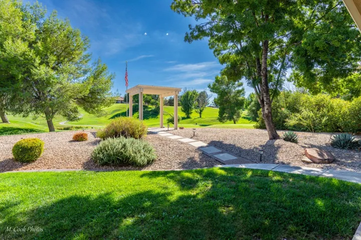 Landscaped backyard featuring a stone pathway, a white pergola, and mature trees