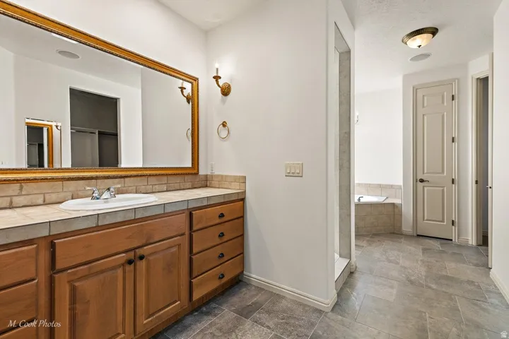 Vanity with wood-finish cabinetry, tile countertop, and an integrated sink