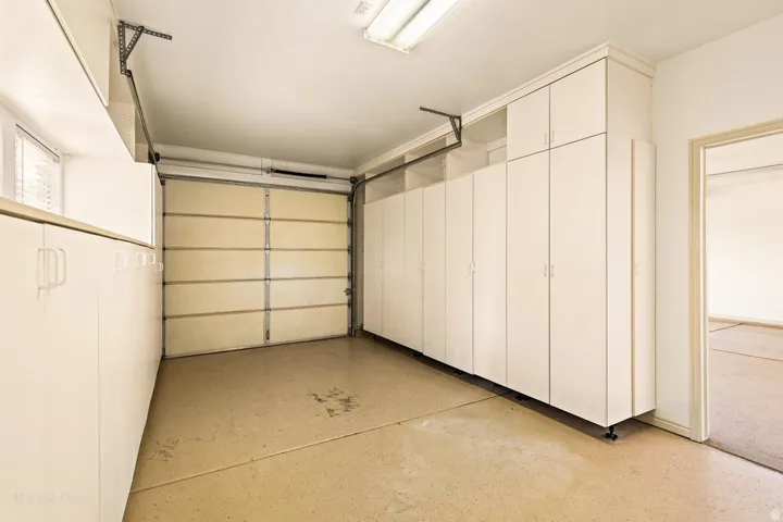 Garage featuring extensive white cabinetry, overhead storage, a single garage door, and light-colored flooring