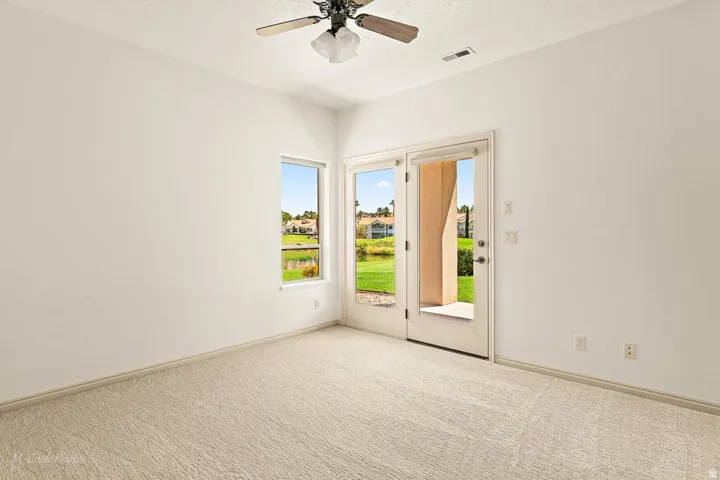 Wall-to-wall carpeting, white painted walls, a ceiling fan, a window, and a glass-paneled door