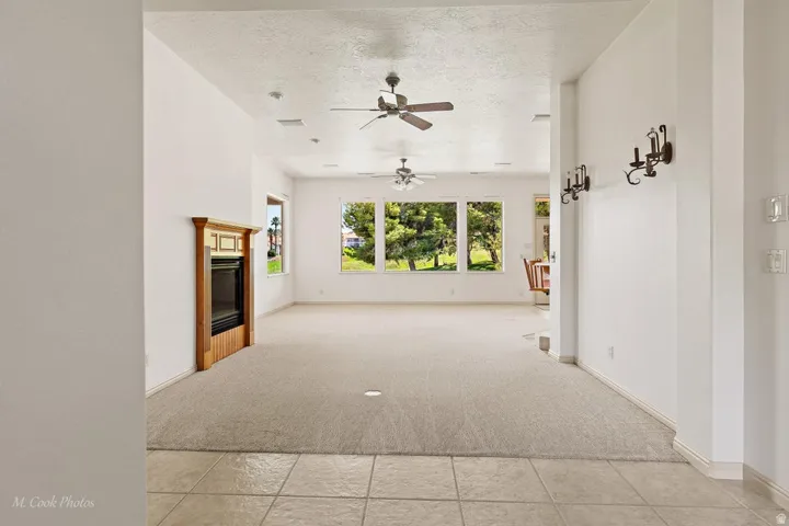 Integrated fireplace with wood mantel surround, multiple ceiling fans, wall-mounted sconce lighting, tiled entryway flooring, and carpeting throughout the living area