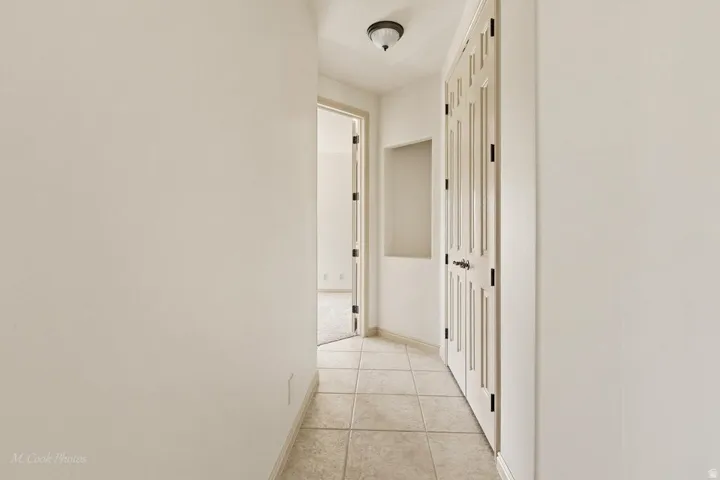 Hallway featuring neutral-toned tile flooring, recessed wall niche, and panel doors with dark hardware