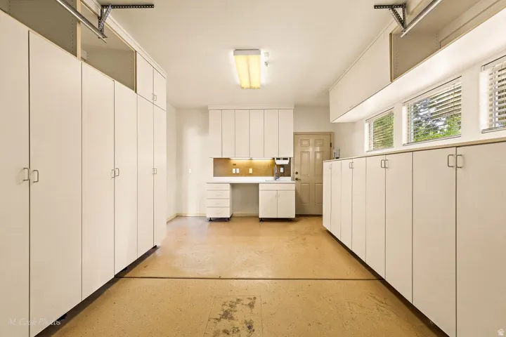 Spacious garage featuring extensive built-in cabinetry, integrated workstation, utility sink, and multiple windows