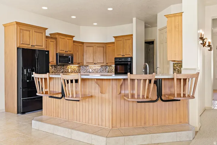 Chef's kitchen featuring warm wood cabinetry, granite-style countertops, stainless steel appliances, and a large island with seating for multiple guests