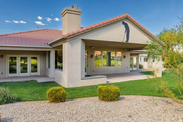 Stucco exterior with a terracotta tile roof, featuring a covered patio, multiple windows, and exterior French doors