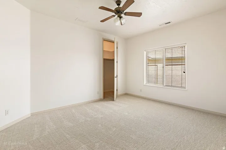 Neutral carpeted flooring, white walls, ceiling fan, and a window with horizontal blinds