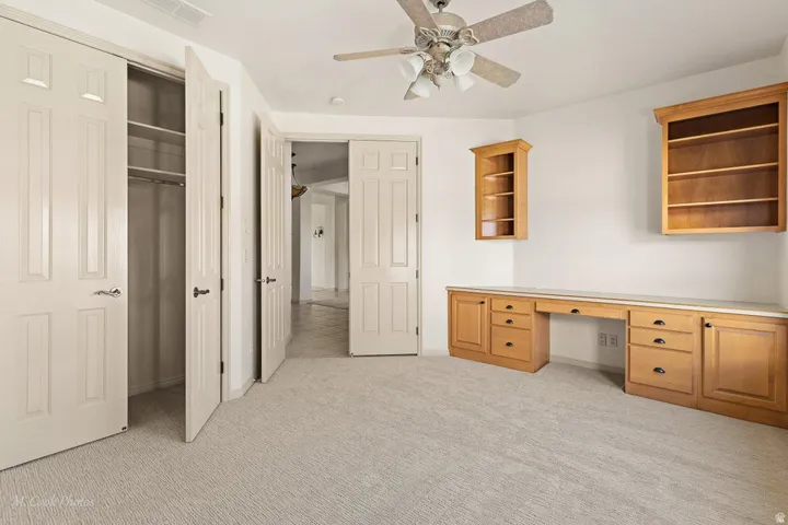 Built-in desk with wood-finish cabinetry, two mounted shelving units, and a ceiling fan with integrated lighting