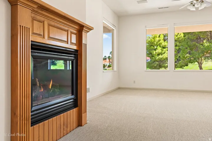 Built-in fireplace with wood-finish surround, multiple windows, and a ceiling fan with integrated lighting