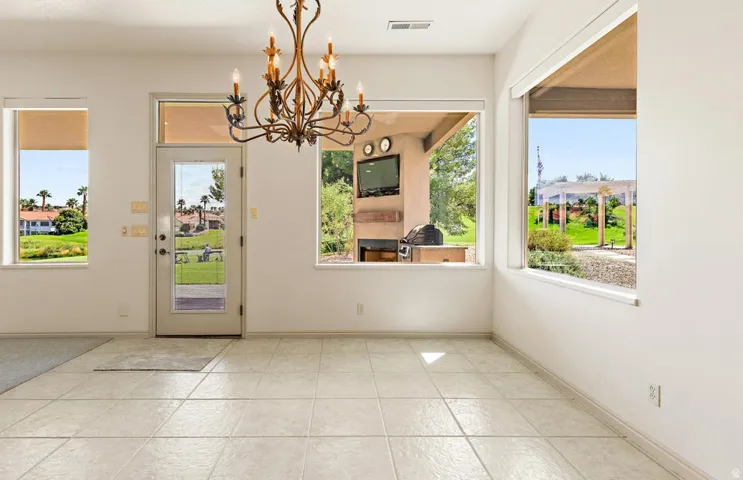 Spacious room featuring light-toned tile flooring, multiple windows, a full-lite glass door, and an ornate chandelier