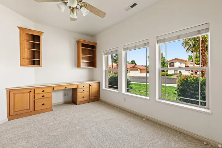 Built-in desk with extensive cabinetry, two wall-mounted shelving units, and multiple windows with blinds