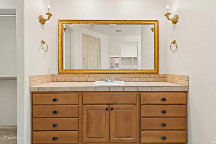 Wood-finish vanity with ample storage drawers, tiled countertop, integrated sink, and an ornate framed mirror