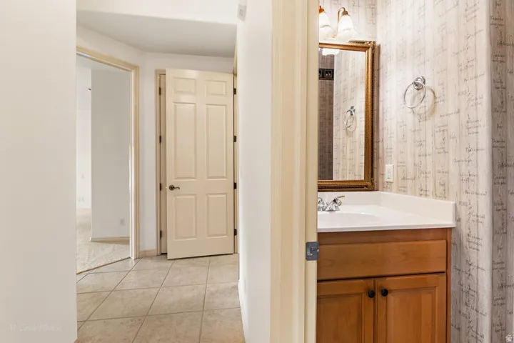 Hallway with neutral tile flooring, leading to a room with carpet flooring