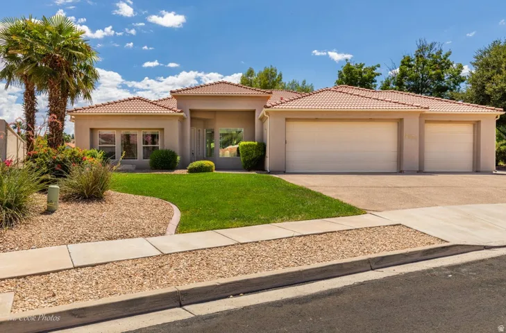 Stucco exterior with a tile roof, mature palm trees, manicured lawn, and a three-car garage