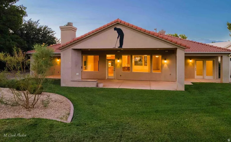 Stucco exterior with a tiled roof, multiple outdoor patios, mature landscaping, and an expansive lawn