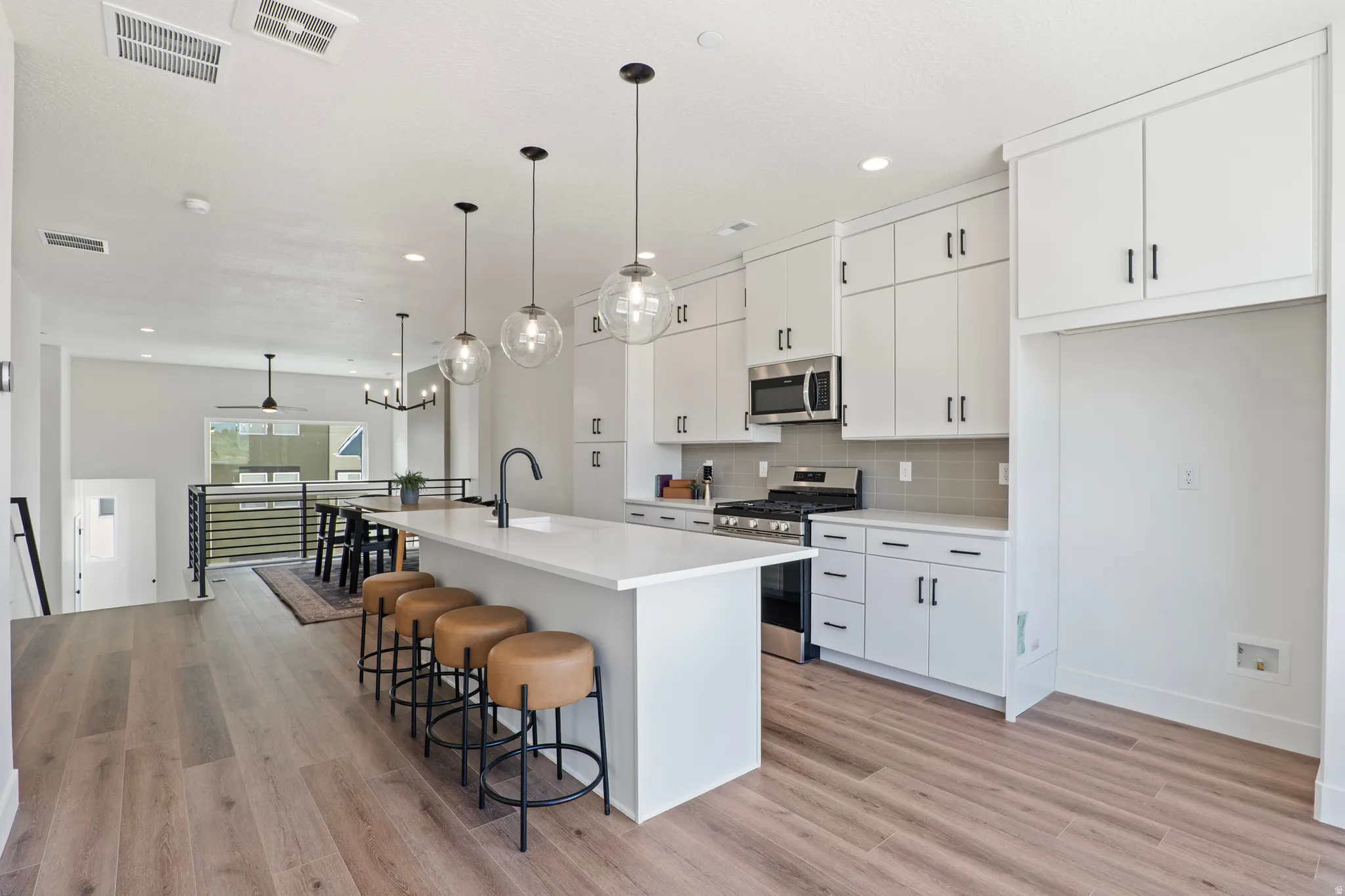 Open-concept kitchen featuring an island with pendant lighting, integrated stainless steel appliances, white cabinetry, and wood-finish flooring
