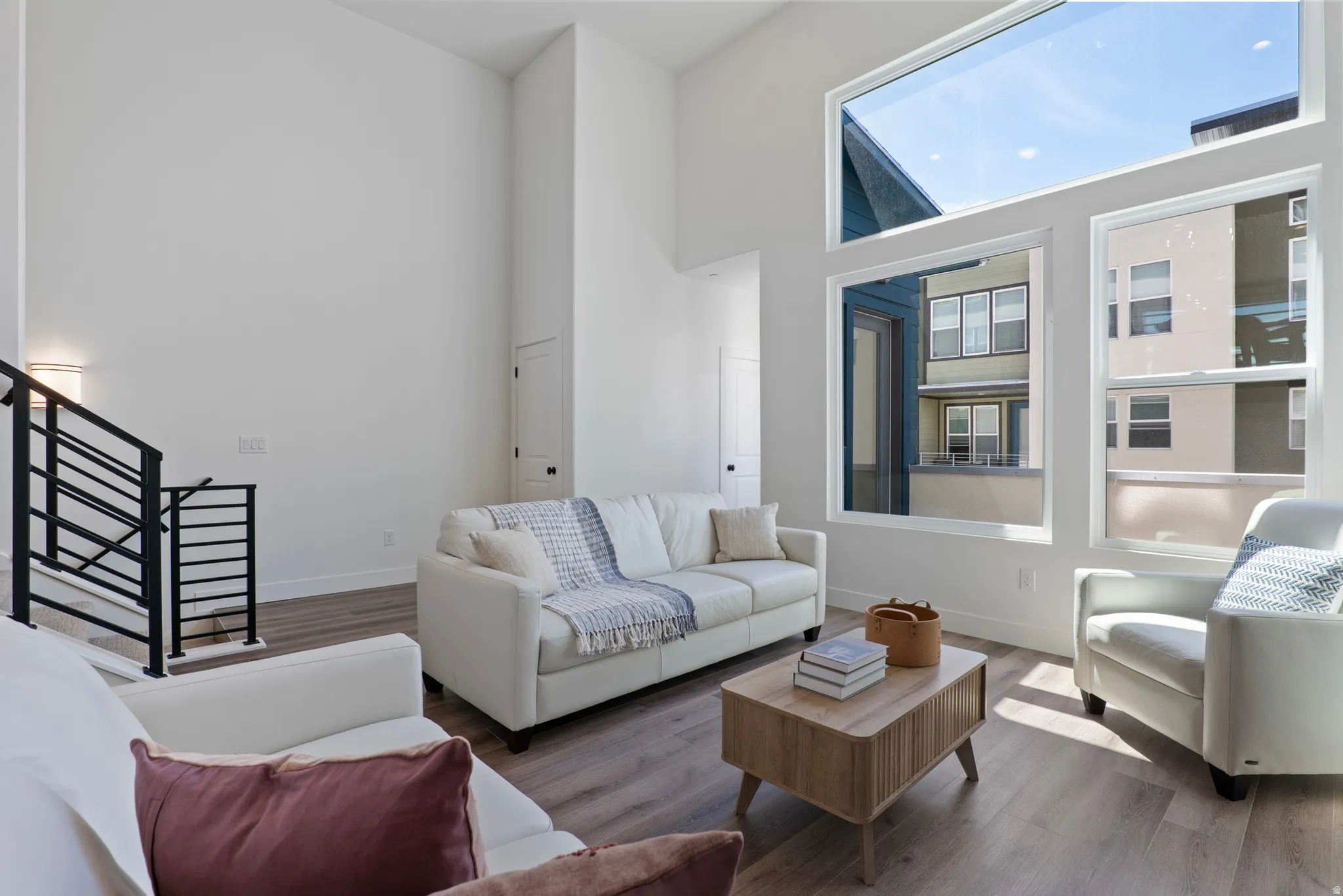 Expansive room featuring high ceilings, wood-finish flooring, a contemporary staircase with metal railings, and large windows providing abundant natural light