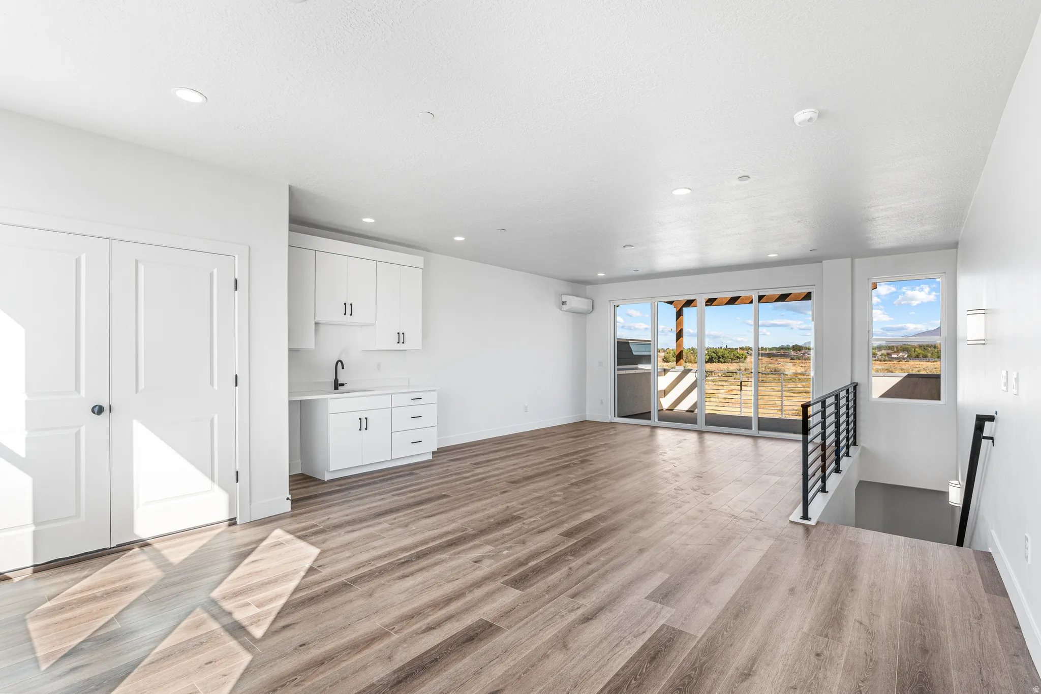 Wood-finish flooring, built-in white cabinetry with a sink, recessed lighting, expansive glass sliding doors, and a metal staircase railing