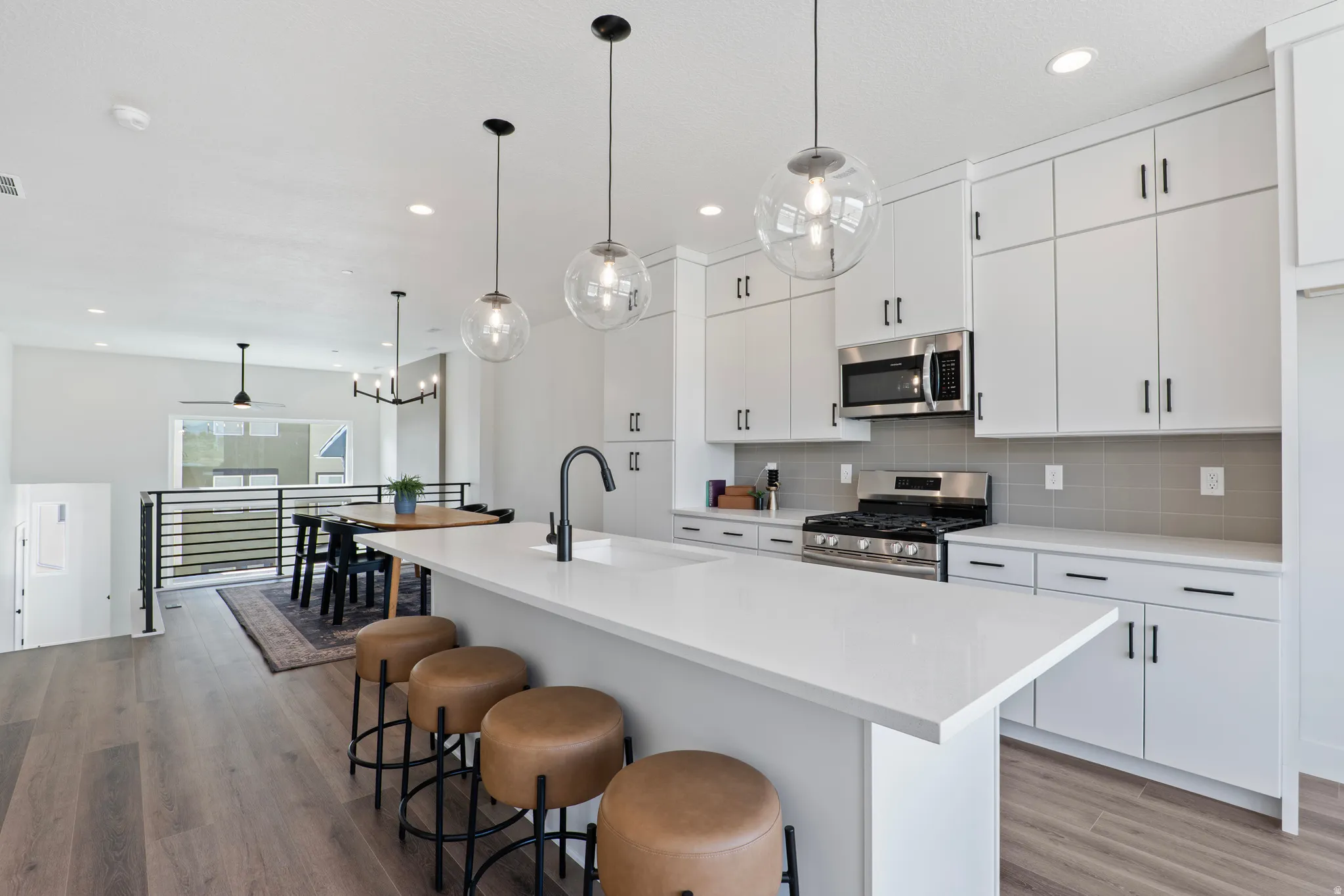 Modern kitchen featuring white cabinetry, stainless steel appliances, a large center island, wood-finish flooring, and pendant lighting