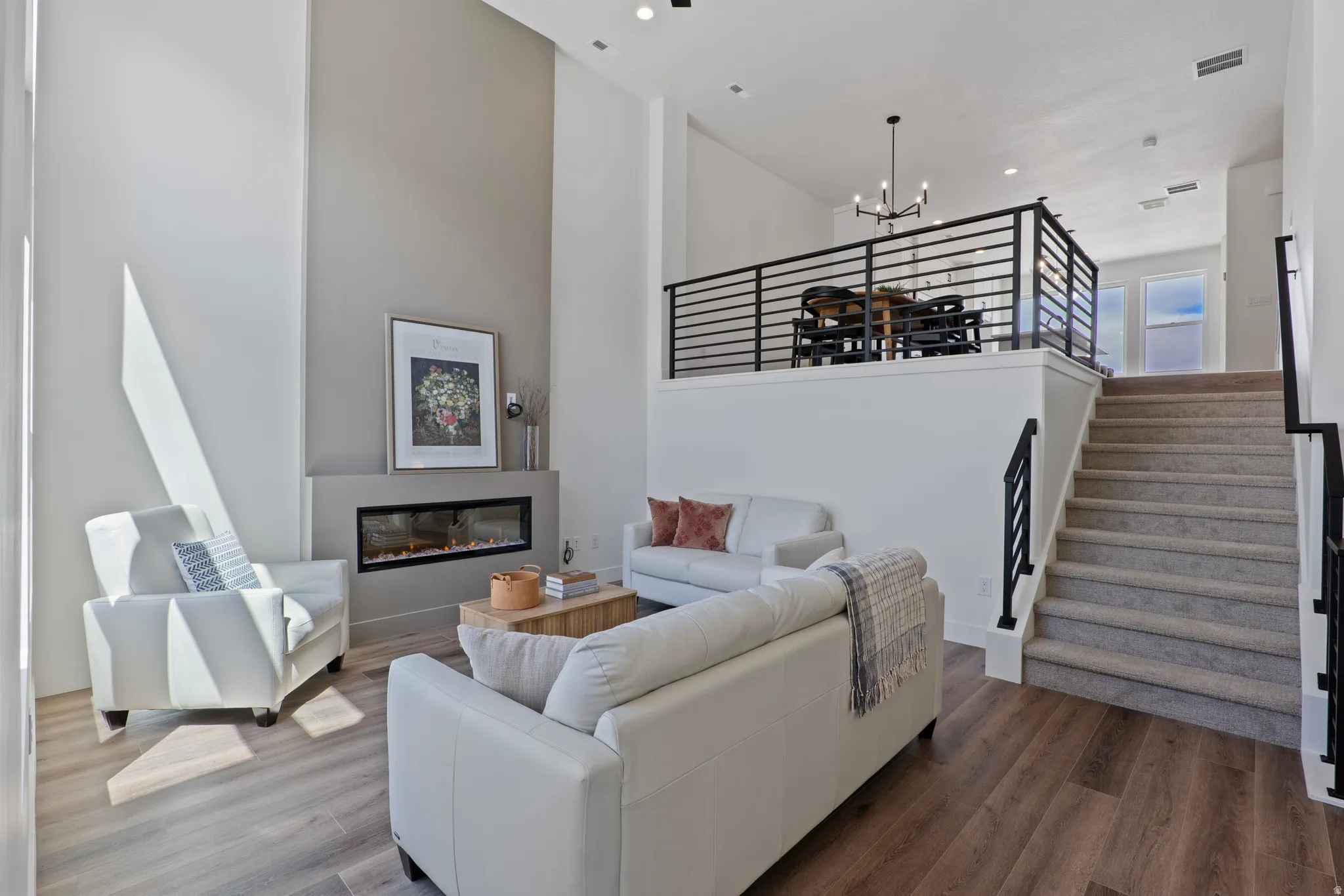 Two-story living area with wood-finish flooring, a linear electric fireplace, and a recessed ceiling