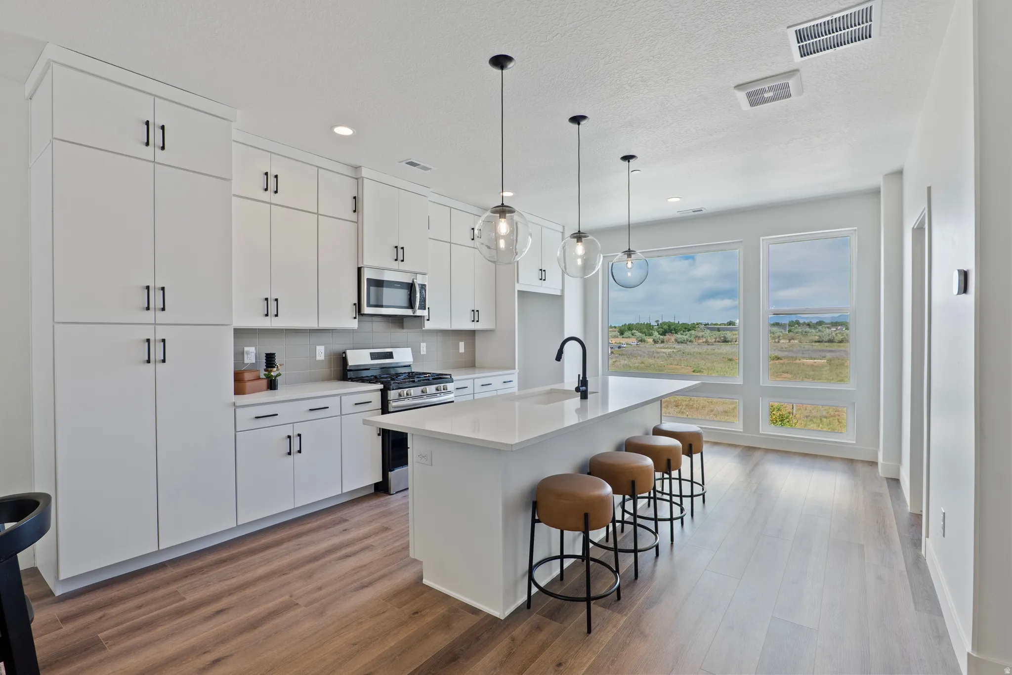 Contemporary kitchen with extensive white cabinetry, a large center island, wood-finish flooring, and expansive windows