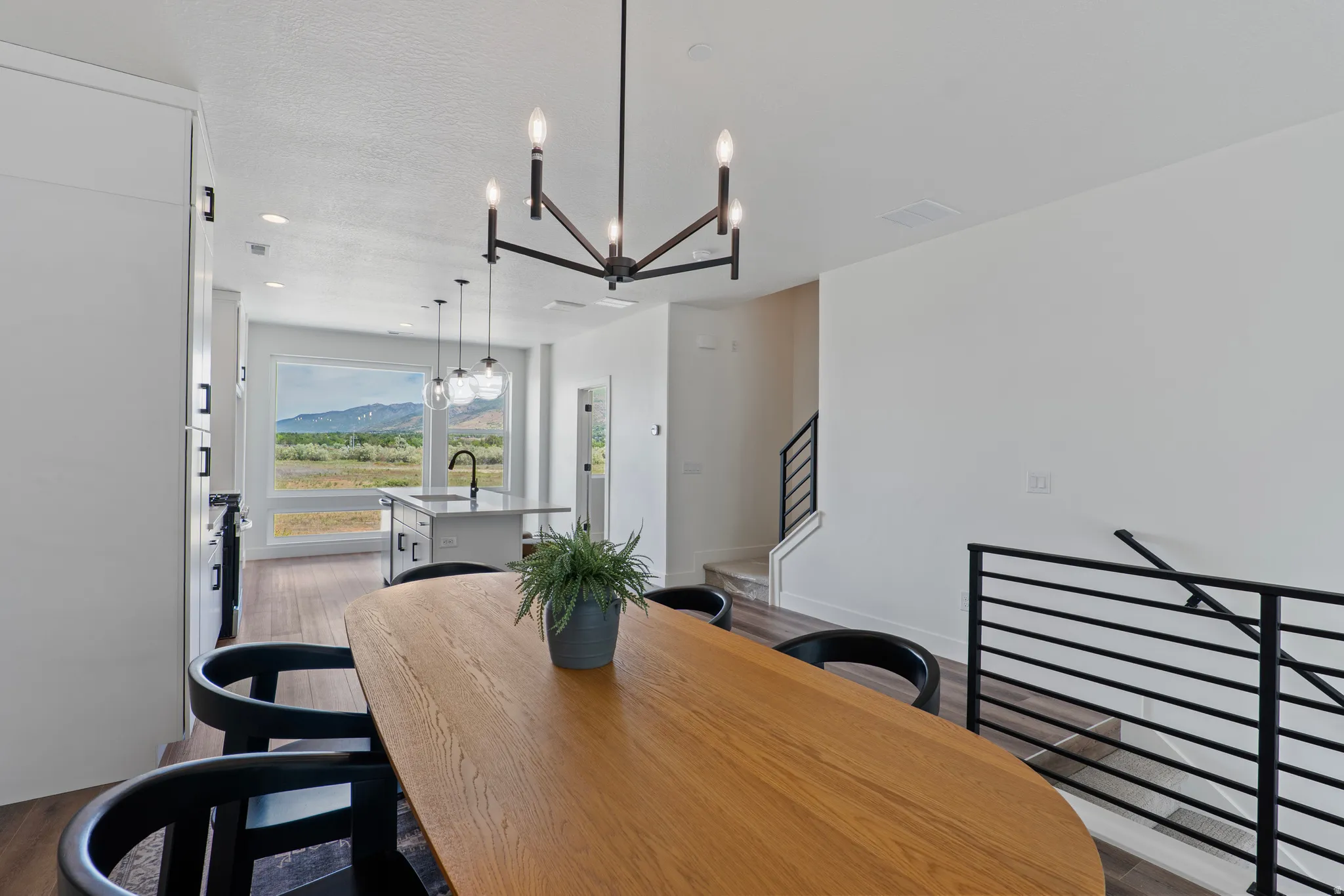 Open-concept living area with wood-finish flooring, a contemporary chandelier, and a large picture window showcasing a distant mountain range