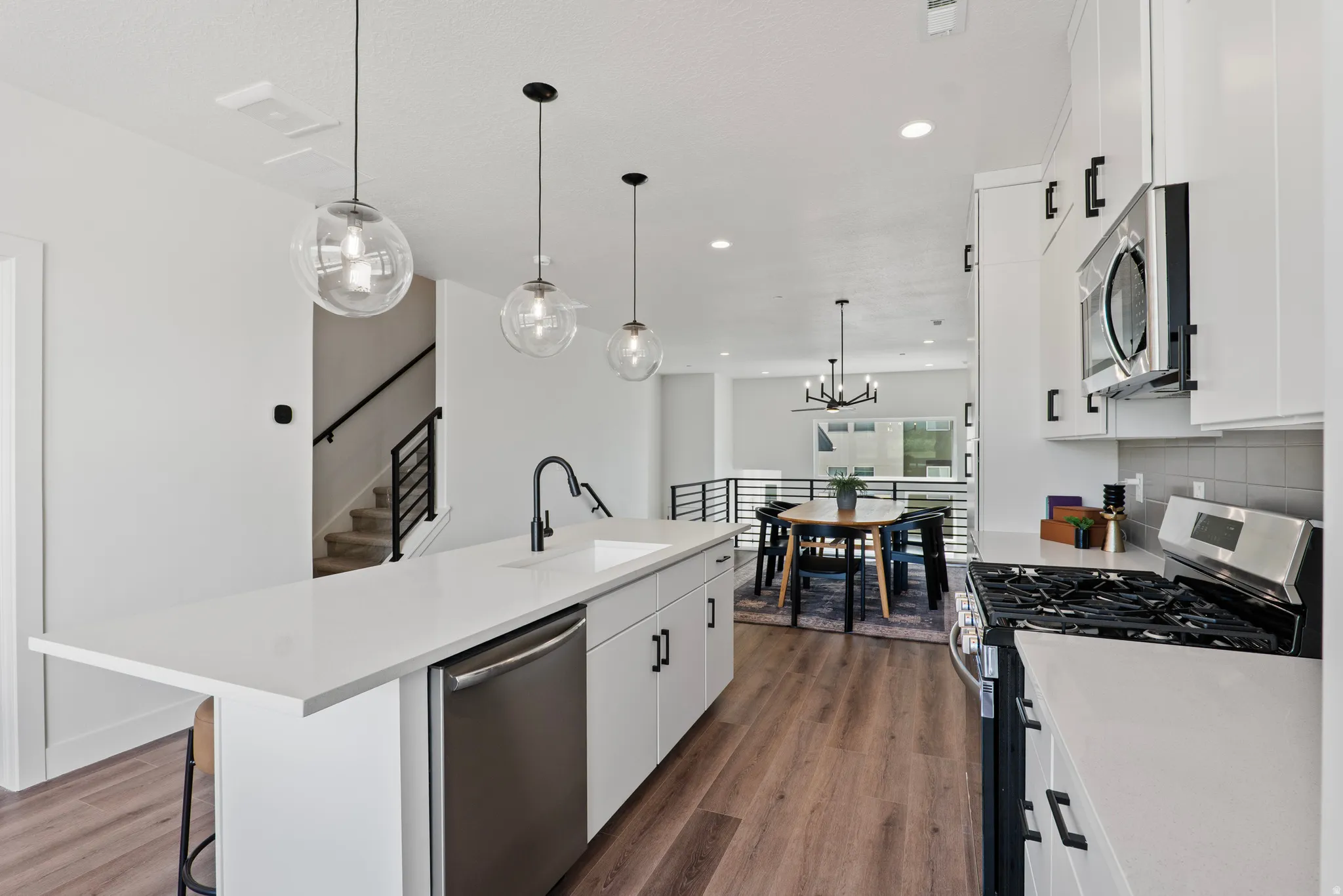 Modern kitchen featuring white cabinetry, stainless steel appliances, wood-finish flooring, and pendant lighting