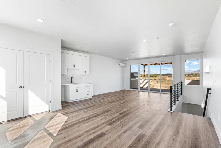 Wood-finish flooring, built-in white cabinetry with a sink, recessed lighting, expansive glass sliding doors, and a metal staircase railing