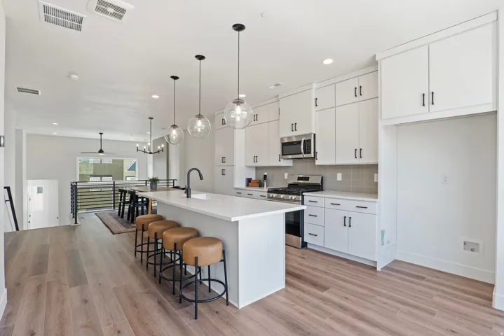 Light, bright, and designed for gathering, this spacious kitchen features crisp white cabinetry, abundant storage, a large center island with seating, modern pendant lighting, and a gas range. Expansive windows bring in natural light and showcase the surr