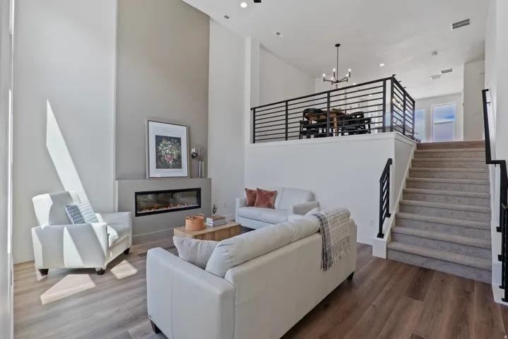Two-story living area with wood-finish flooring, a linear electric fireplace, and a recessed ceiling